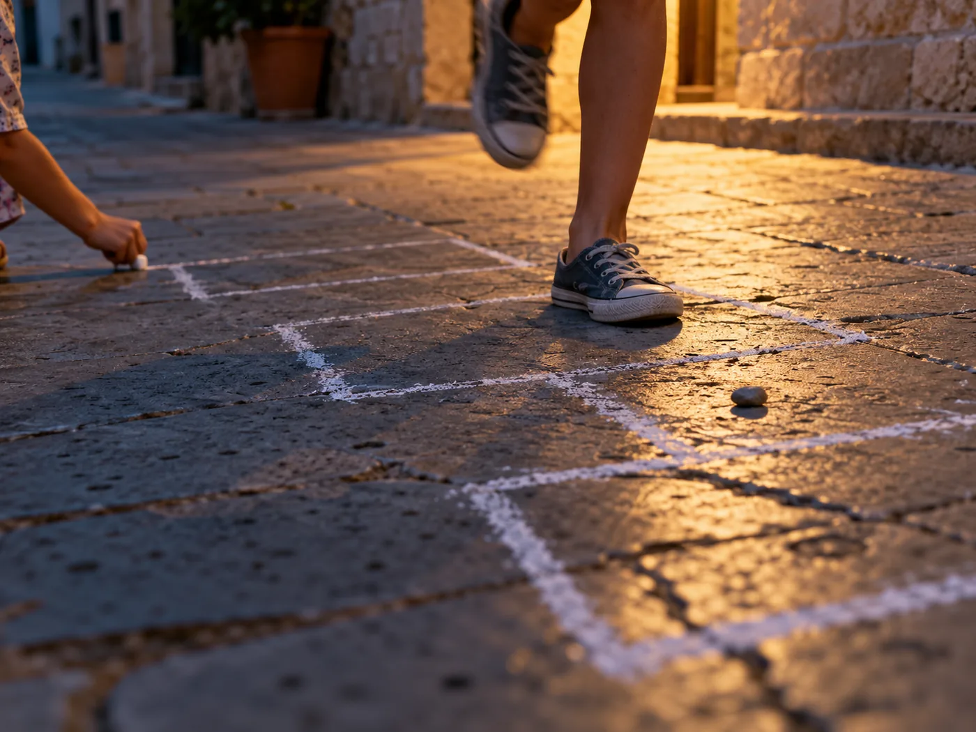 A child hops across a chalk hopscotch game on the pavement at dusk.