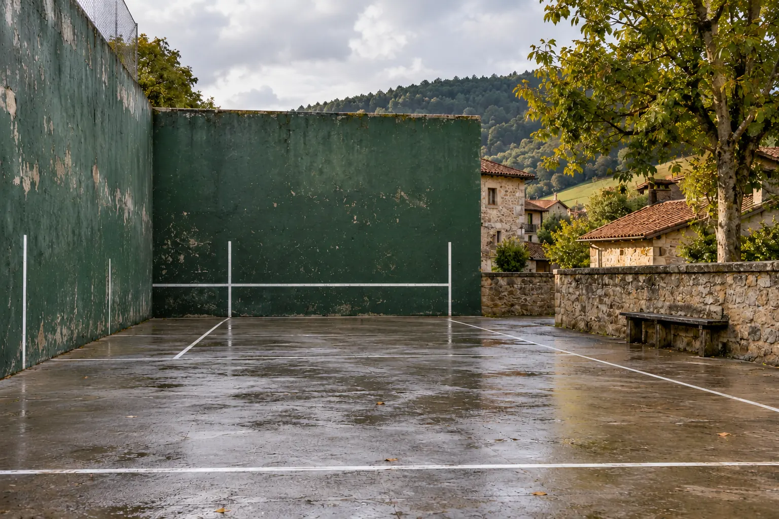 An open-air frontón with a green front wall and the side wall on the left.